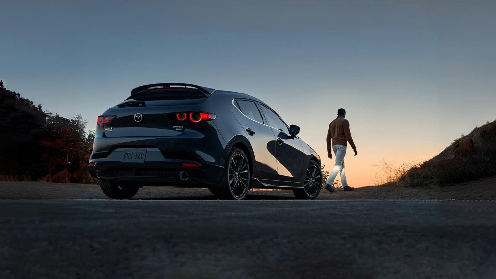 black mazda 3 hatchback, back view with driver walking off into the sunset