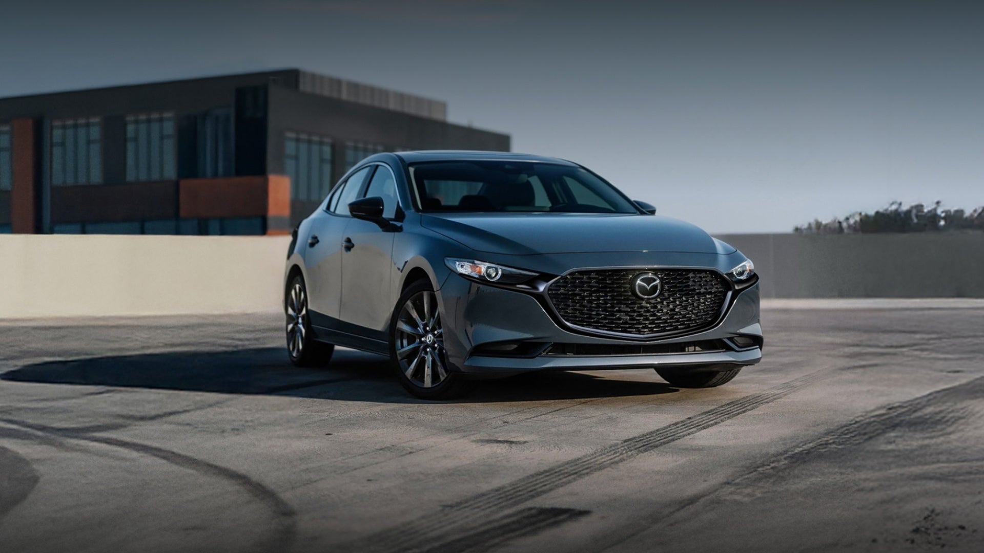 A Mazda 3 parked in a lot, showcasing its sleek design and modern features under clear blue skies.